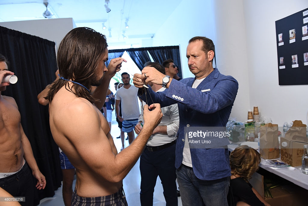 Designer Erik Nelson assists a model backstage at the Edinger Apparel presentation during New York Fashion Week; Image via Gettyimages.com